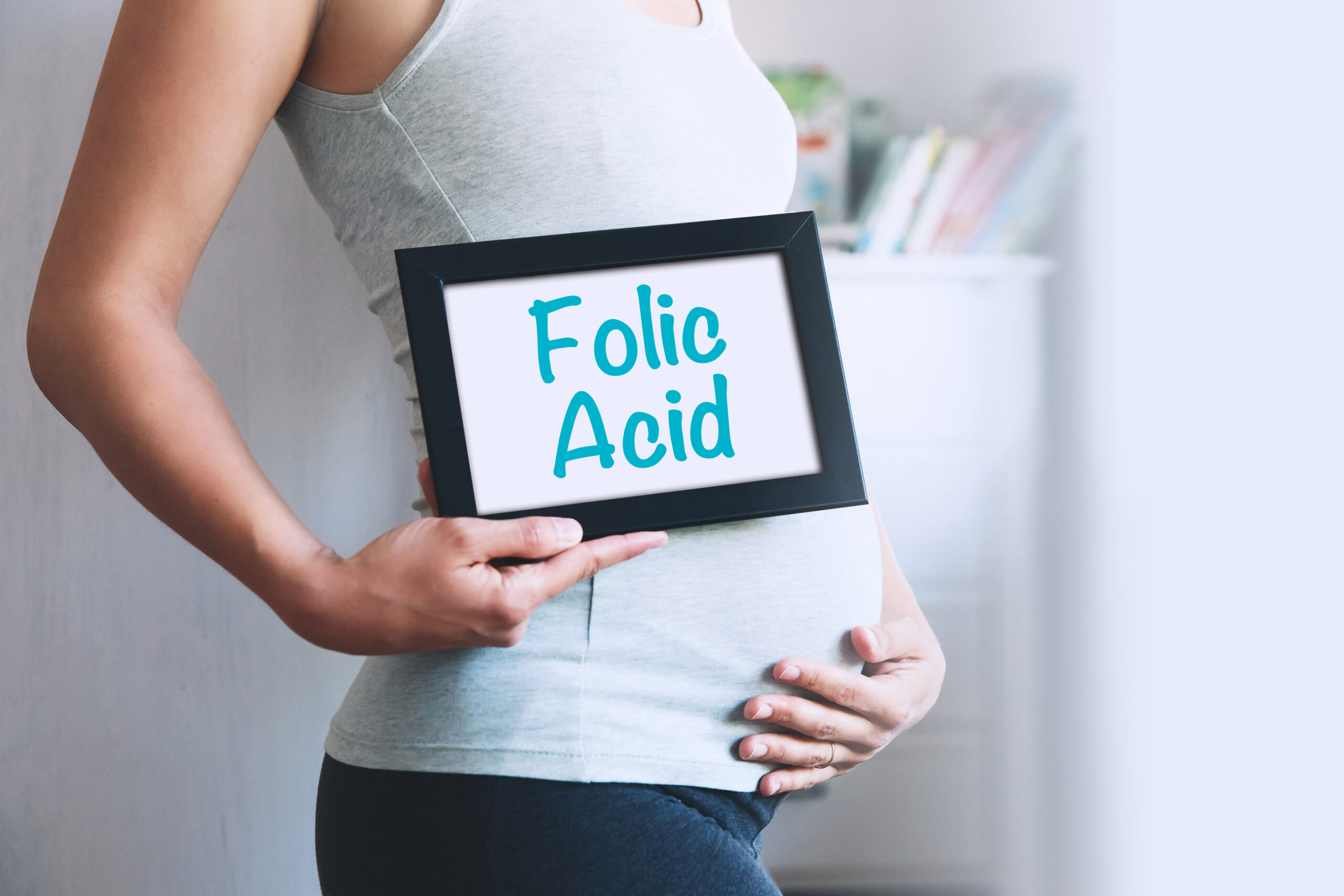 A pregnant woman holds a whiteboard, on which is written: folic acid.