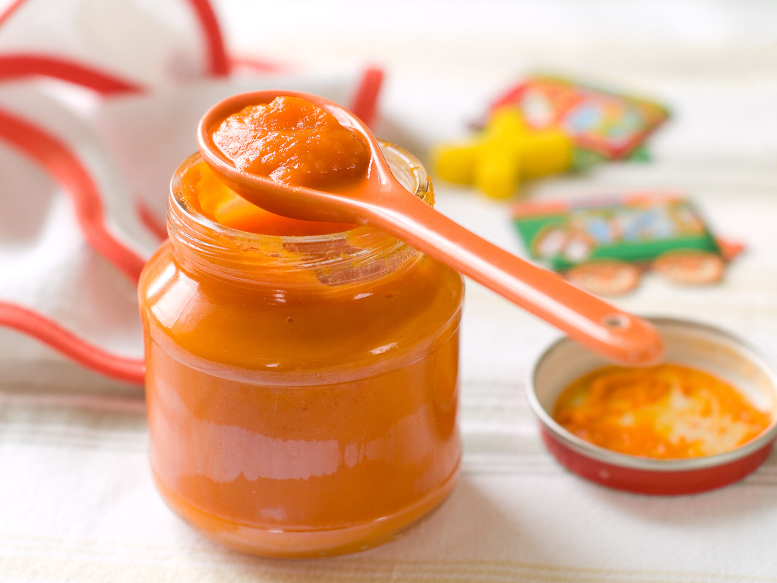 Baby food. A jar of orange pureed baby food with a spoon resting on its lip.